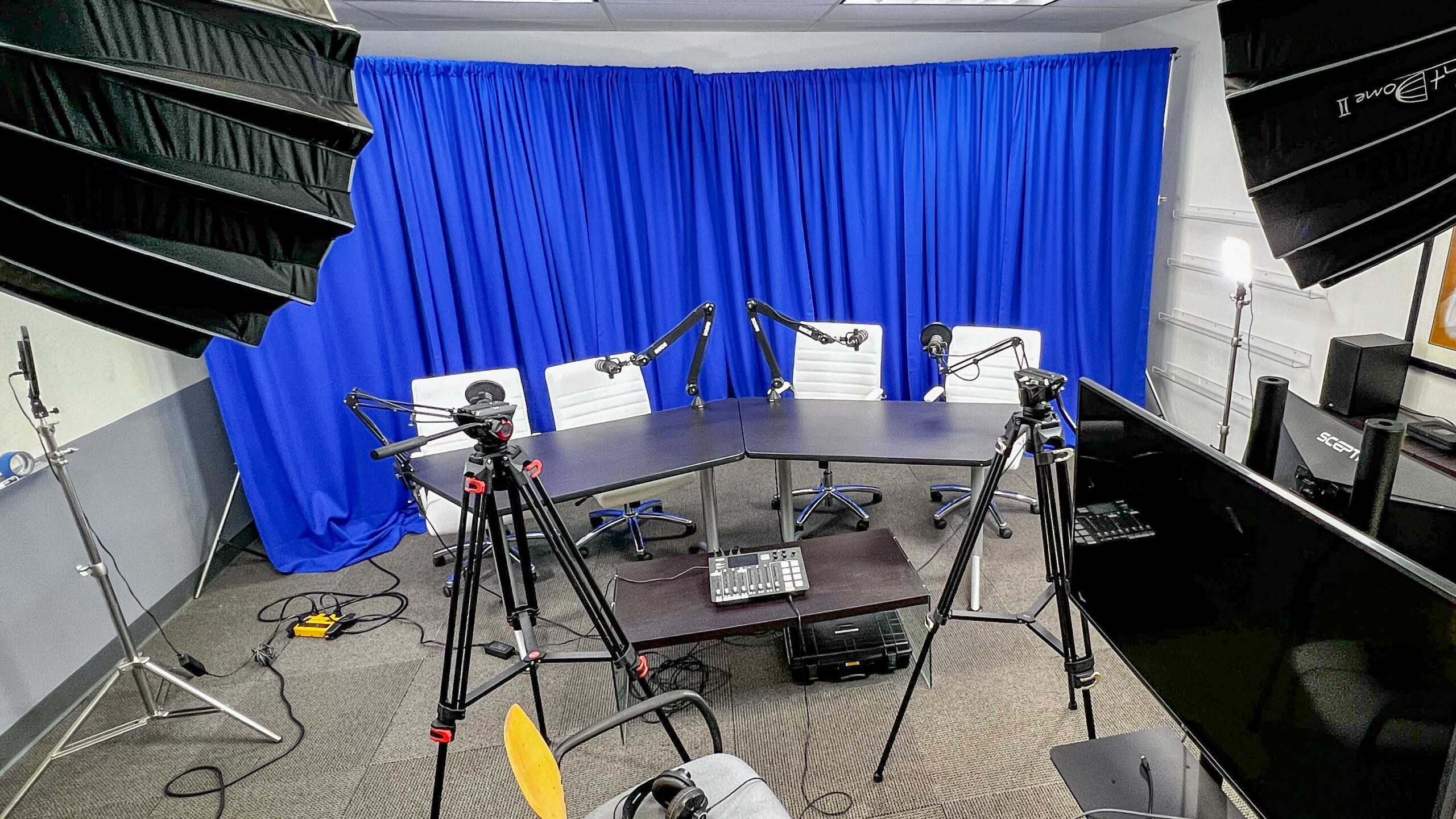 A full podcast set up with microphones, cameras, a sound board, background, lights, and monitors.