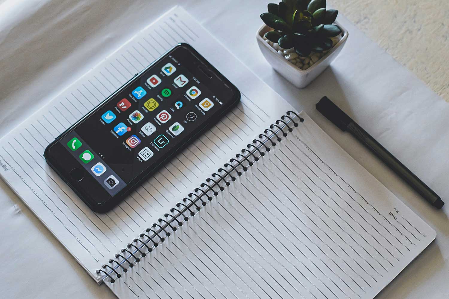 A phone laying on a notebook with a pen laying next to them.