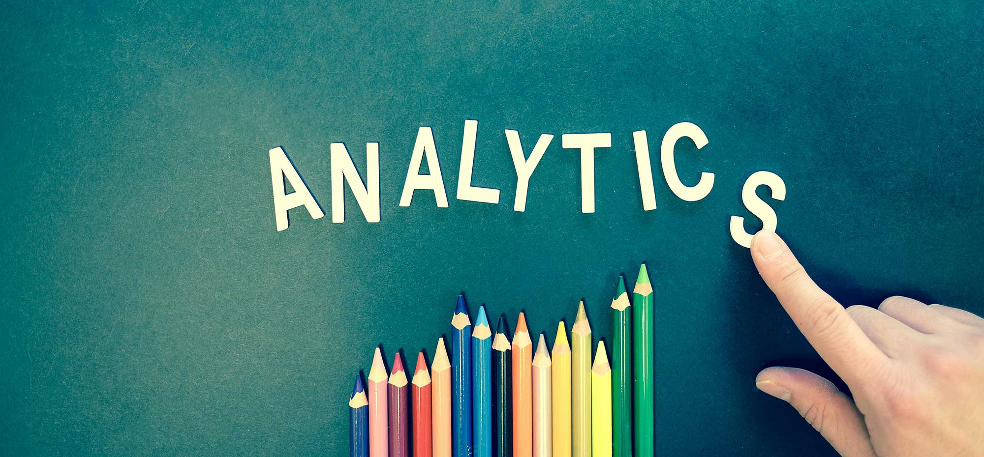 Analytics spelled out with colored pencils below and a hand placing the "S" at the end.