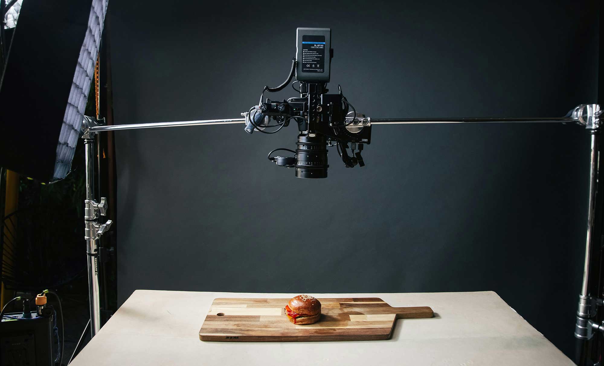A camera being held in suspension films a burger on a cutting board from above.