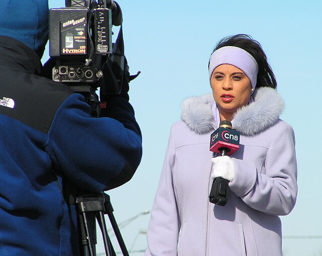 A reporter holding a microphone in front of a camera.