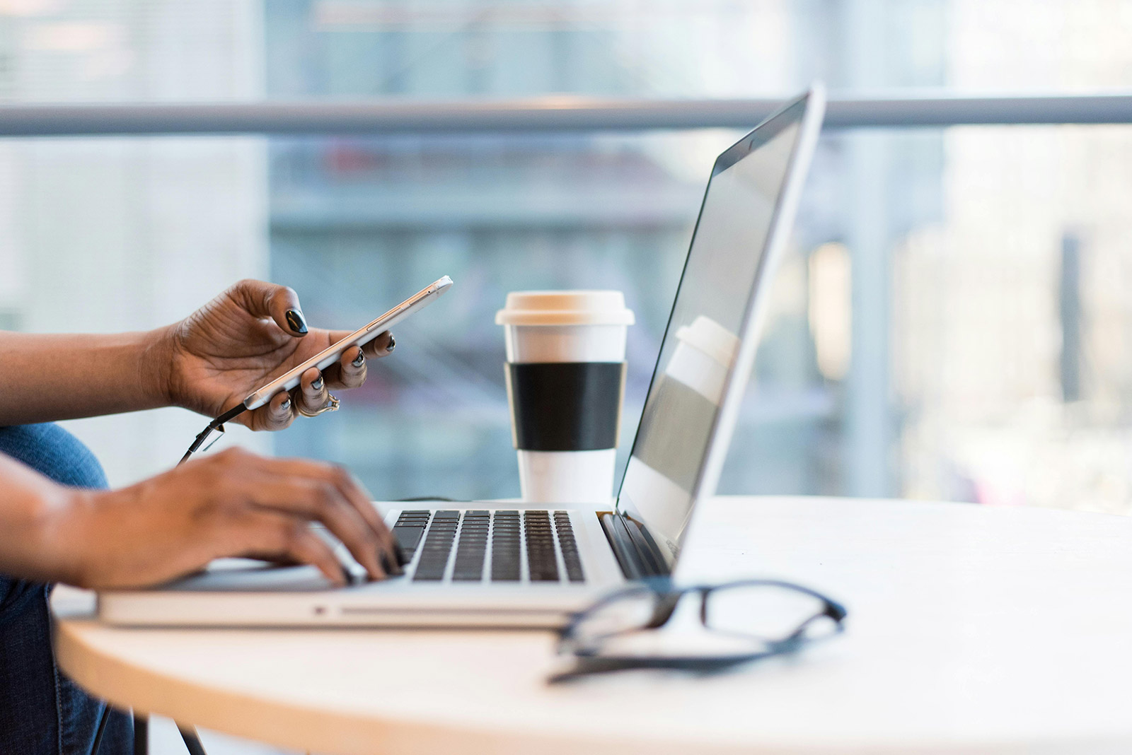 A laptop, phone, coffee, and glasses on a table while a marketer works.